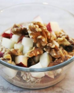 a glas dish with overnight oats topped with apple and walnuts