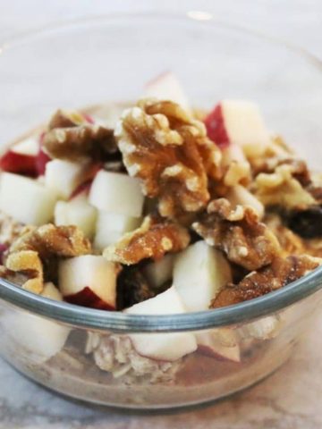 a glas dish with overnight oats topped with apple and walnuts