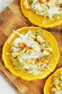 top view of a butternut squash round topped with pesto, melted parmesan and toasted pine nuts