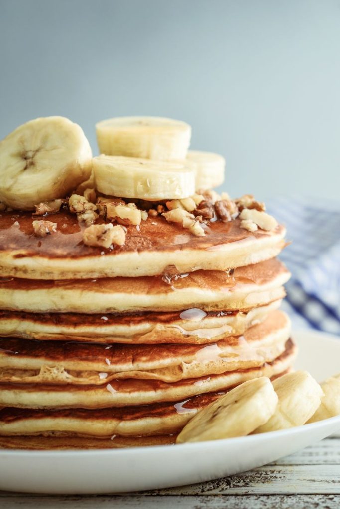 profile view of a stack of pancakes with slices of bananas and syrup