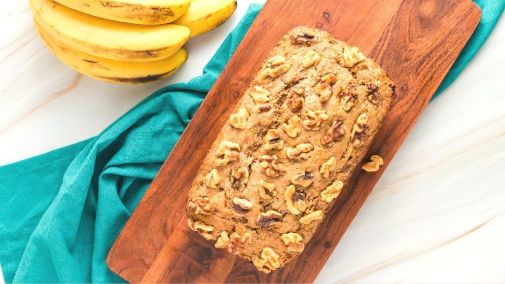 top view of the cooked loaf of banana bread on a wooden cutting board with a turquoise napkin
