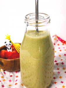 side view of a green smoothie in a glass milk jug with a metal straw
