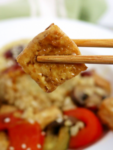 a fried tofu square being held by a chopstick