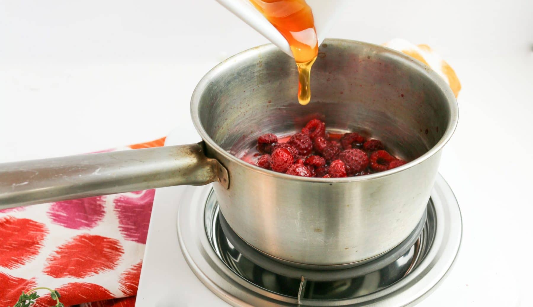 pouring honey into pot of frozen berries