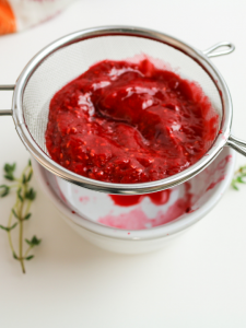 red berry puree in a strainer over a white bowl
