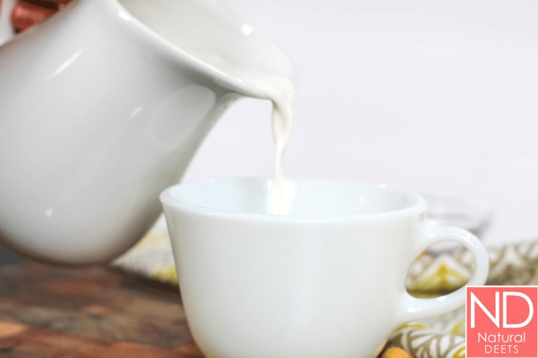 a picture of cashew milk being poured from a carafe into a white coffee cup