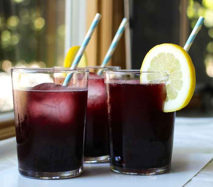 a dark purple drink in a glass garnished with a straw and lemon