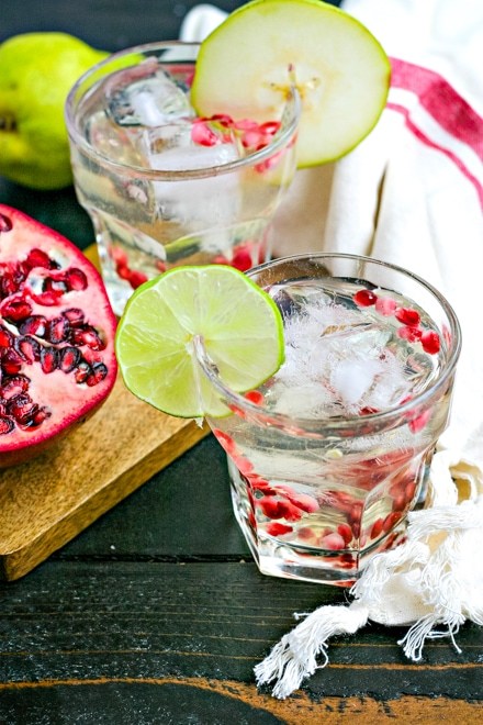 glass with white liquor and sprinkled with pomegranate seeds and garnished with a lime round