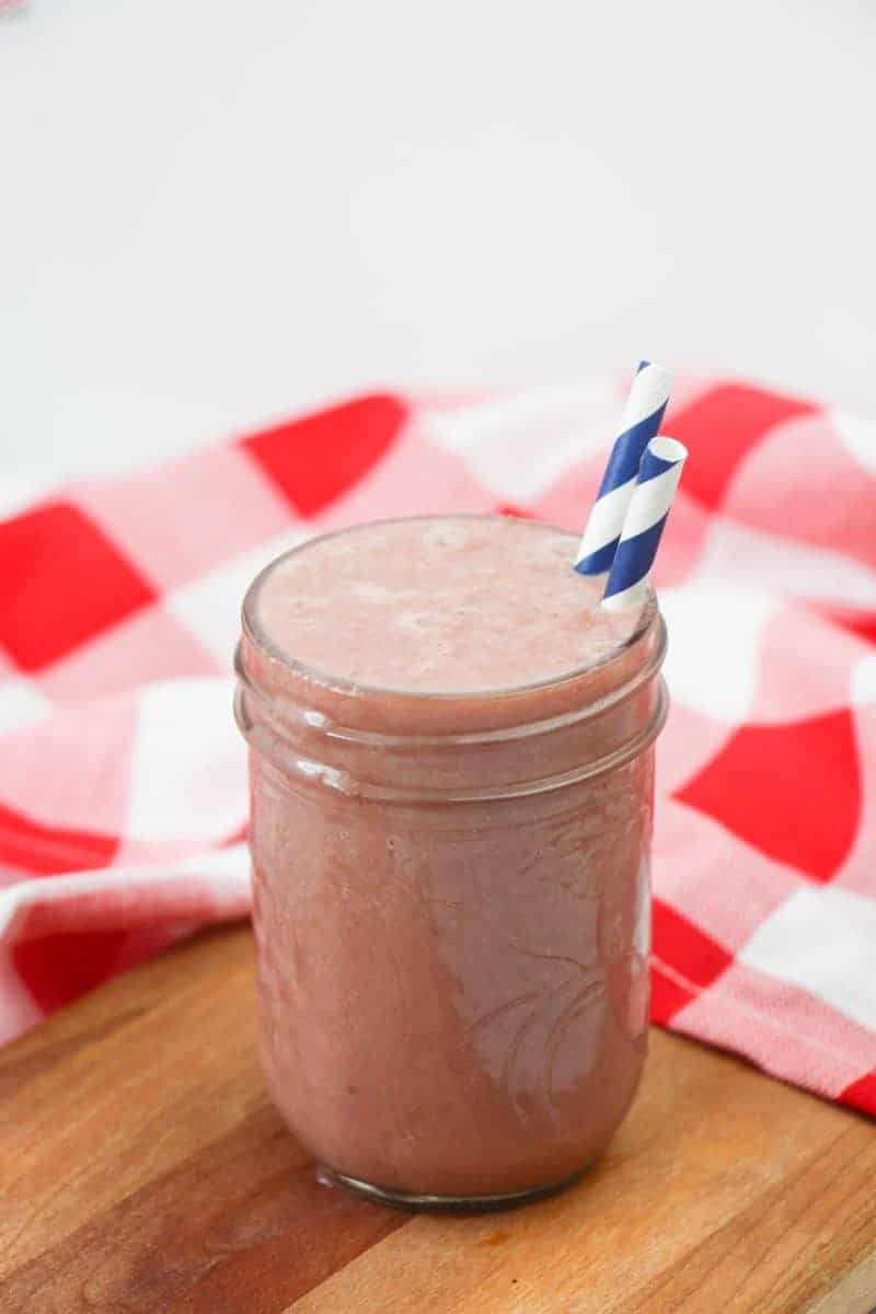 side view of a pink smoothie with a green straw on a red adn white checkered napkin