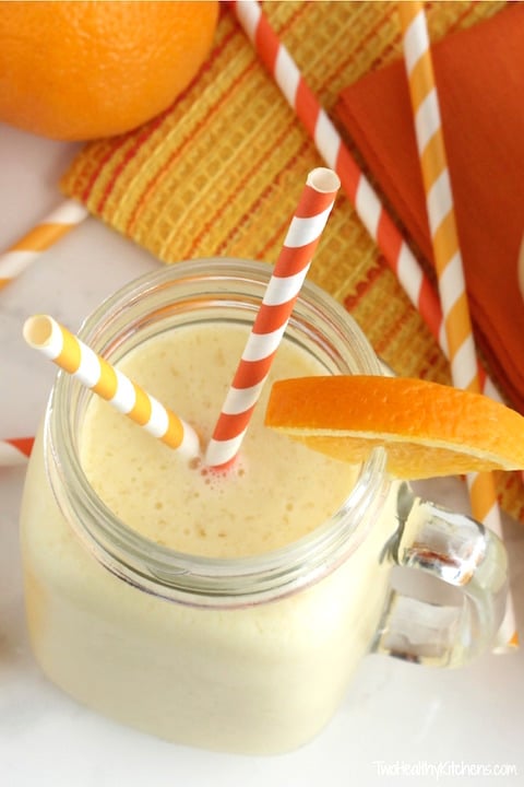 an orange frothy smoothie in a glass mason jar with 2 straws and an orange garnish