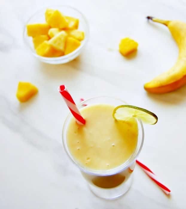 a top view of on orange smoothie with a red straw garnished with frozen mangoes