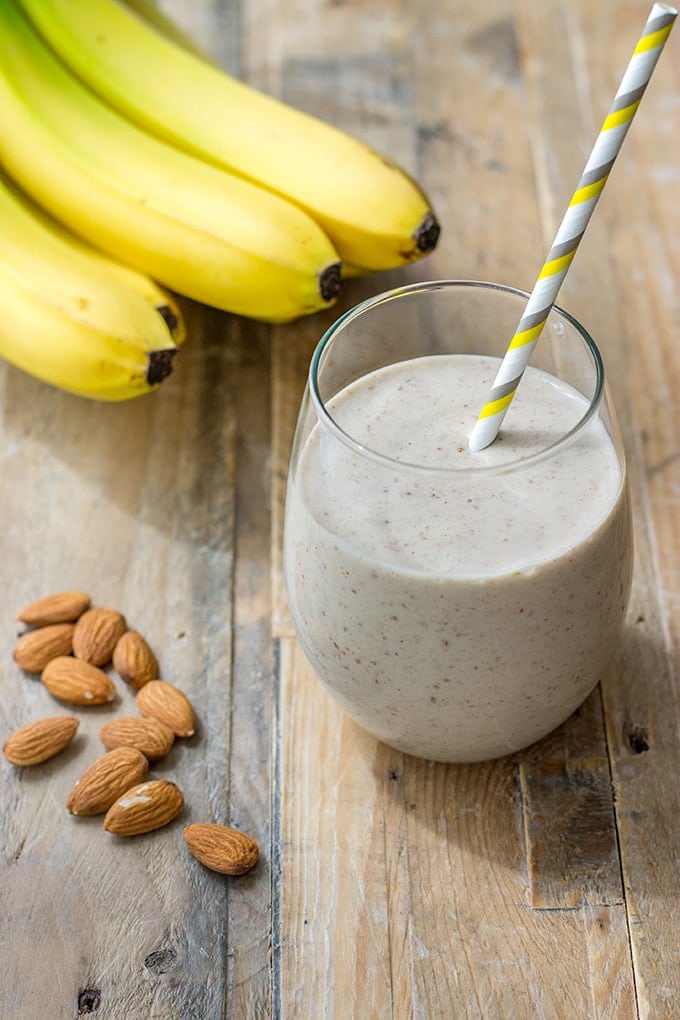 a picture of a white smoothie with bananas and almonds on a wooden cutting board