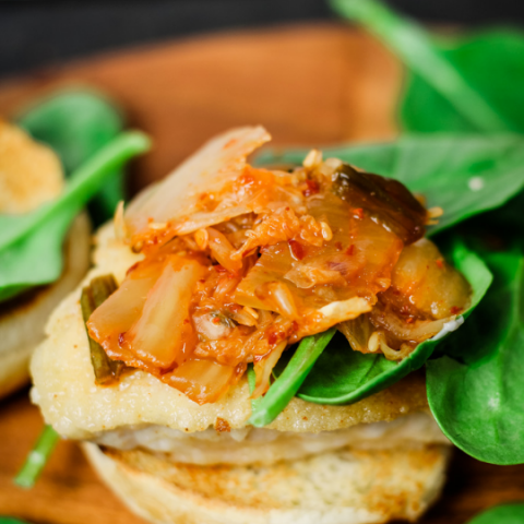 a bottom hamburger bun, pan fried chicken patty and topped with spinach and kimchi