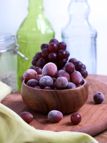 frozen grapes in a wooden bowl with fresh grapes in the background