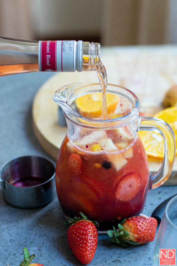 vodka being poured into a pitcher of sangria with strawberries 