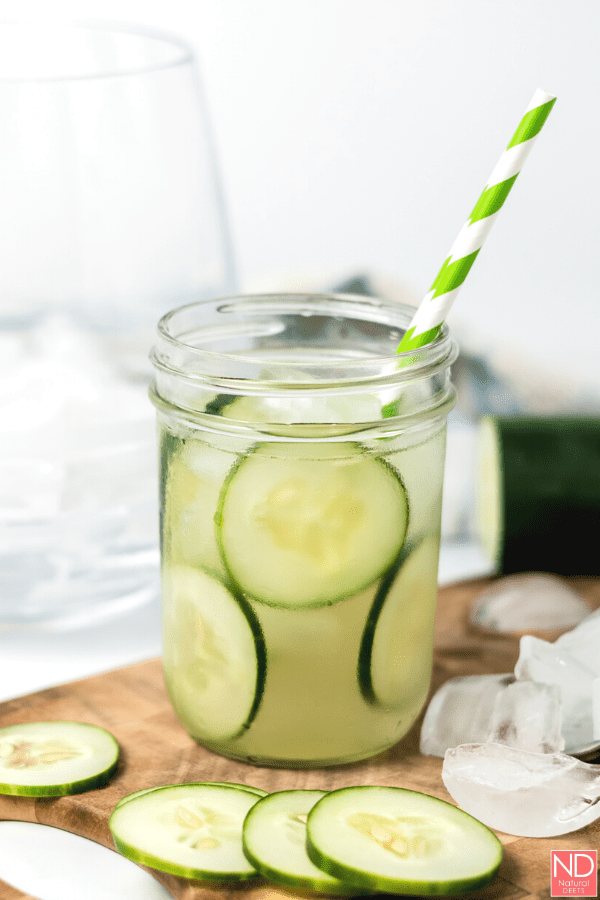 side view of coconut cucumber infused water with round cucumbers and a green striped straw