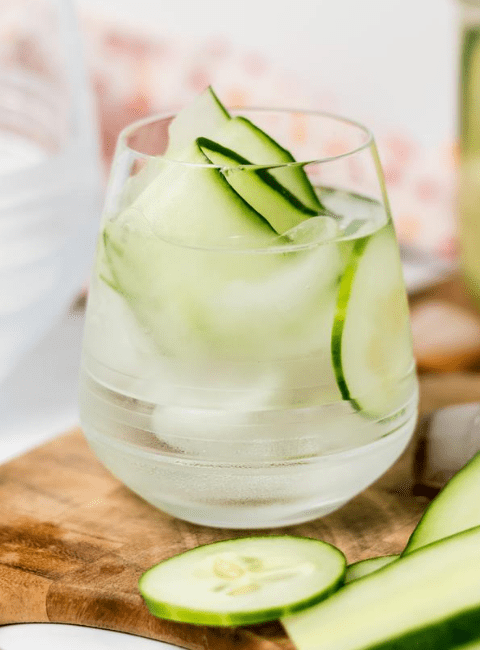 side view of a glass with water, ice and cucumber ribbons