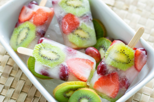 a white rectangle dish with ice and popsicles. The popsicles have kiwi and strawberry slices