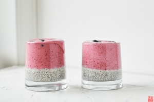 a side view of two cups with chia seeds on the bottom half and a berry smoothie on the top
