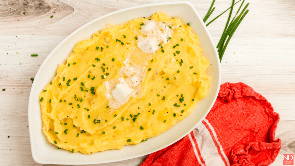 yellow mashed potatoes in a white serving dish with melted butter on the top