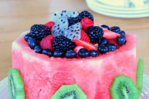 a watermelon cut into a round cake shape and topped with berries and dragonfruit slices