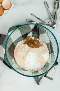 a glass bowl on a black and white plaid towel. the bowl has flour, salt, cinnamon and making soda