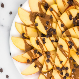 sliced apples on a white plate, drizzled with almond butter and sprinkled with chocolate chips