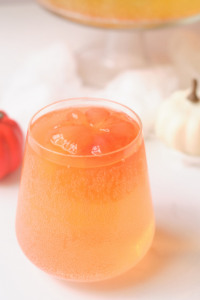 a clear glass with peach colored juice and bright orange pumpkin shaped ice cubes