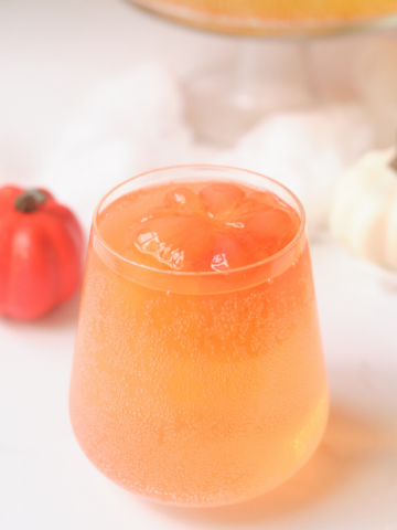 a stemless wine glass with orange colored juice and an orange pumpkin ice cube