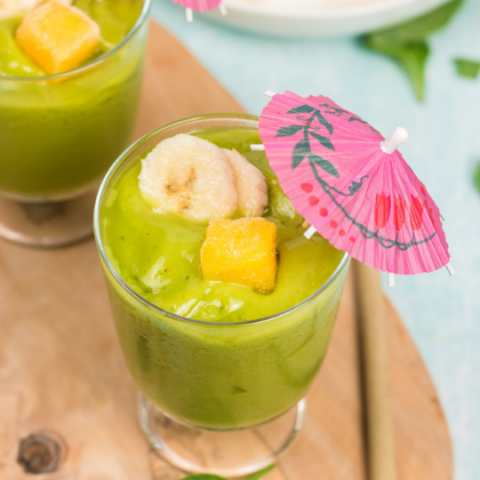 45 degree view of a green smoothie with slices of bananas, a square of mango and a pink unbrella
