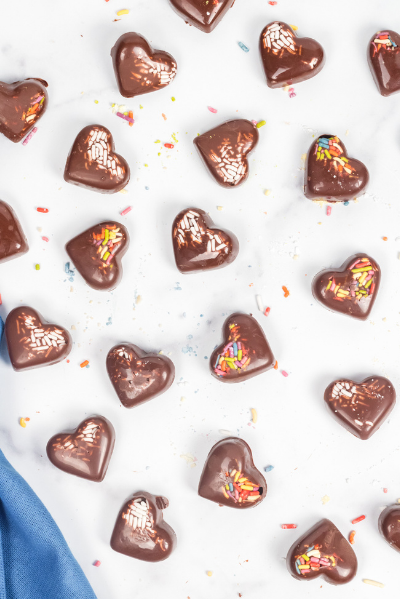 chocolate hearts spread out on a white table with a blue napkin in the lower left hand corner and sprinkles on the table