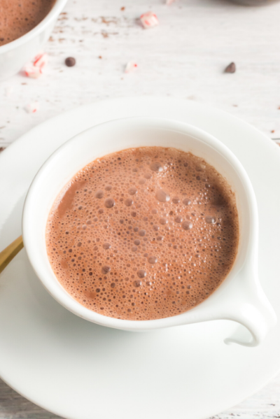 Top view of a white mug on a white saucer filled with hot chocolate and some bubbles on top