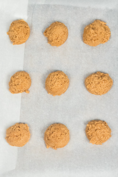 top view of a cookie sheet with 9 round balls of peanut butter cookie dough
