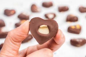 a hand showing the bottom of a chocolate heart where the macadamia nut is showing