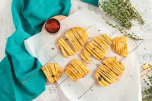 potato slices cut into an accordian shape on a skewer that has been baked to be crispy. Turquoise towel in the left side of the screen