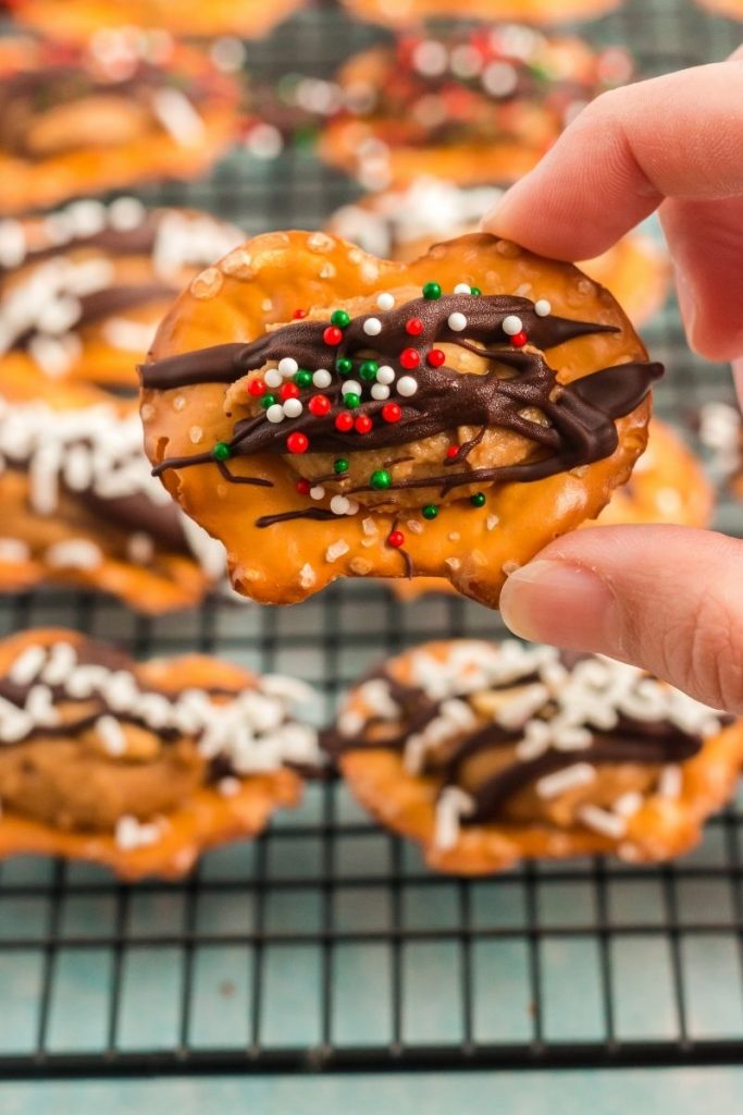hand holding up a pretzel with peanut butter and chocolate drizzle and sprinkles. The pretzel is being held towards the camera to show the top view