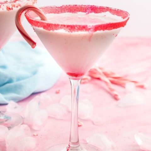 side view of a white cocktail in a martini glass with red sugar on the rim and a candy cane