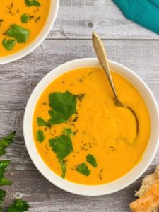 top view of yellow orange pumpkin soup in a white bowth garnished with parsley and a spoon