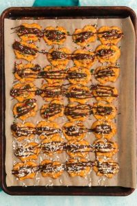 top view of pretzels on a sheet pan with a ball of peanut butter on each one and drizzled with melted chocolate and topped with red, green and white sprinkles