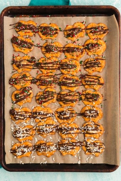 top view of pretzels on a sheet pan with a ball of peanut butter on each one and drizzled with melted chocolate and topped with red, green and white sprinkles