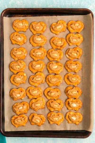 top view of the pretzel crisps on a sheet pan with a ball of peanut butter on each one and a peanut pressed into the peanut butter