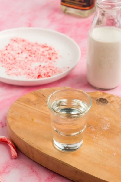 side view of a shot glass with voda, a milk jar iwth half and half and a plate of candy canes