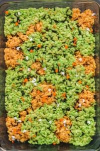 top view of green and orange rice krispy treats pressed into in a pan and spirnkled with white ghots, orange pumpkins and black sprinkles