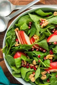 top view of a half a bowl of baby spinach with sliced pears, pomegranate arils and walnuts