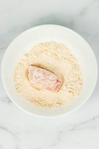 top view of a square chicken breast in a bowl of flour