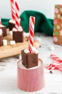 front view of a red and white paper cup turned upside down with a square of chocolate on top and a candy cane spoon in the chocolate