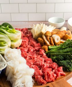 side view of a tray with hot pot ingredients like beef, bok choy, rice noodles and fish cakes