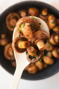Top view of mushrooms in a black pan with a white spoon holding them up
