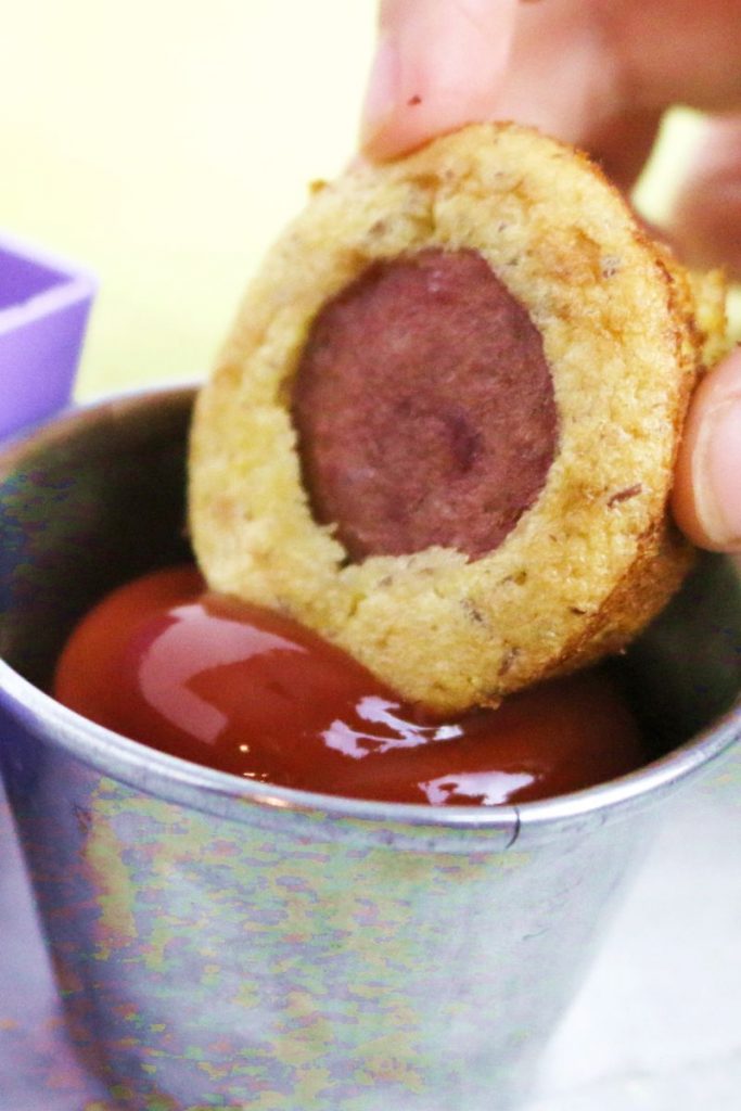 corn dog muffin being dipped into a cup of ketchup