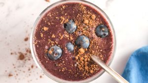 top view of a cup with a brown/blue colored smoothie topped with blueberries and cocoa powder